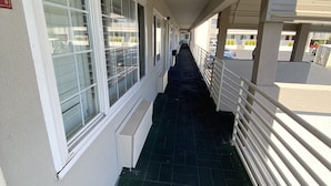 A corridor with a tiled floor, white walls, and large windows with blinds.