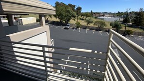 A parking lot with a few cars, a building with a beige roof, and trees in the background. - Budget Inn of Hayward (Hayward)