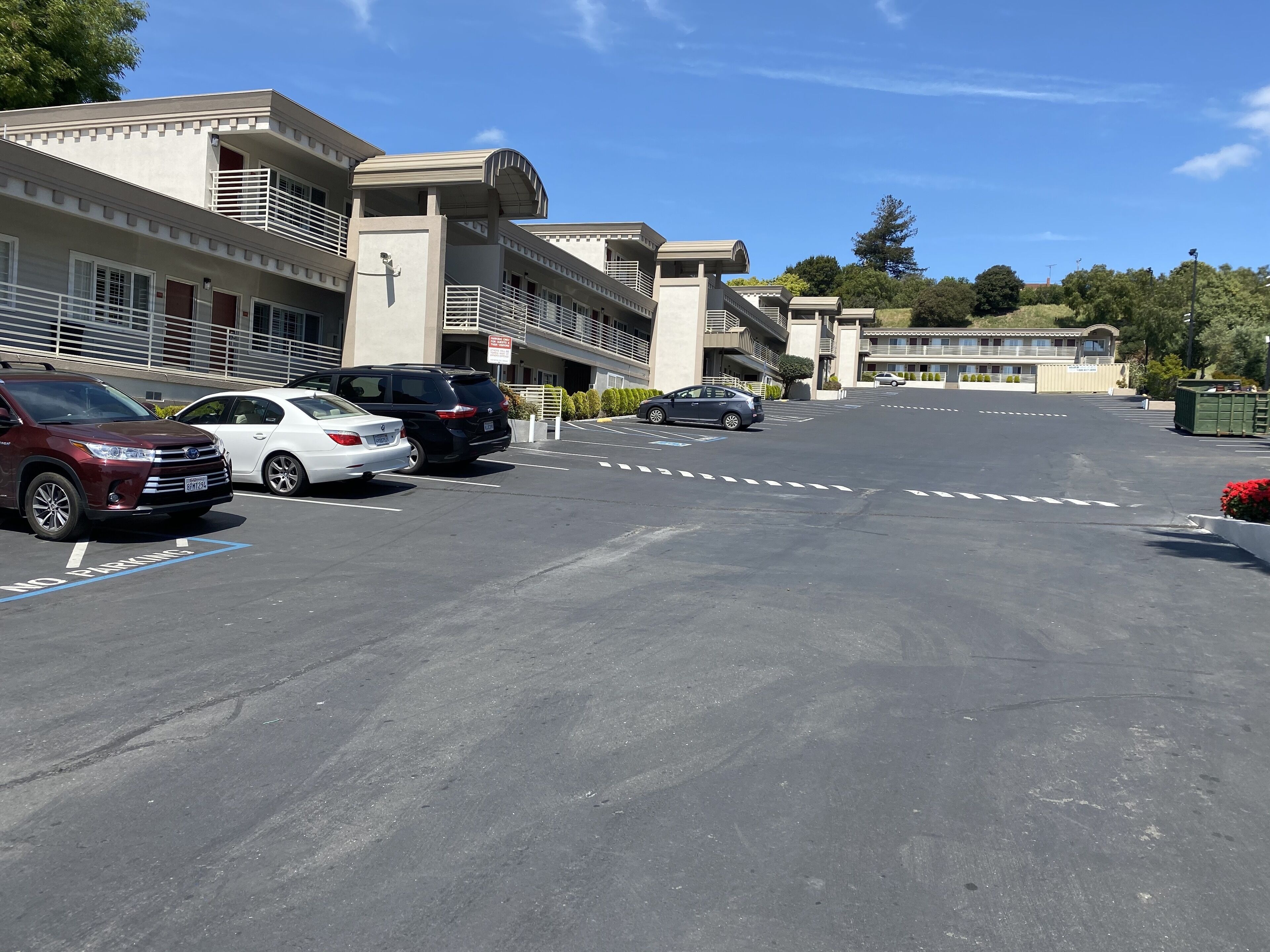 A parking lot with several cars, including a red SUV and a white sedan, in front of a building with a modern architectural style.