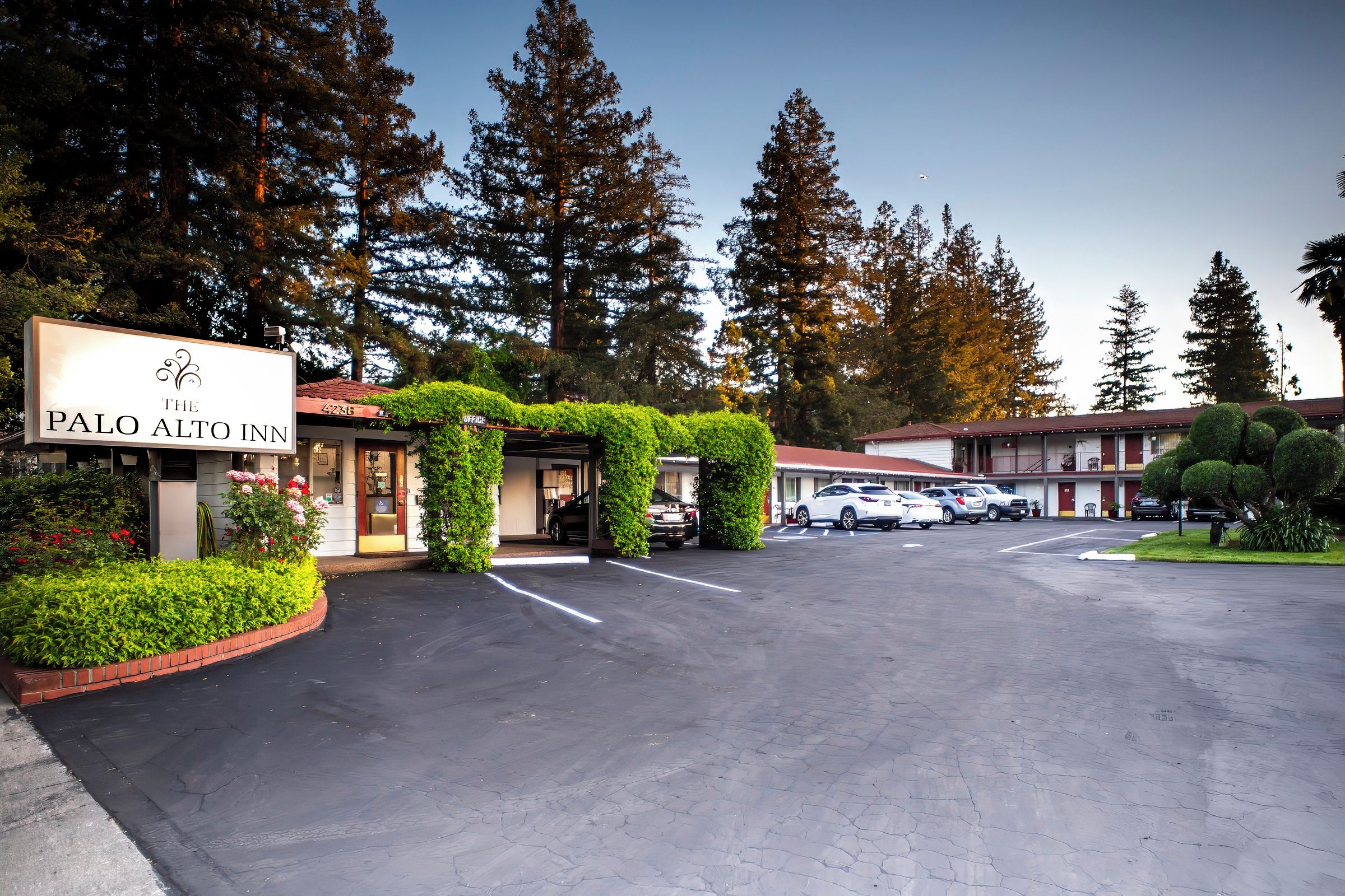 Un estacionamiento con un edificio identificado como 'The Palo Alto Inn' y un letrero con un diseño decorativo.