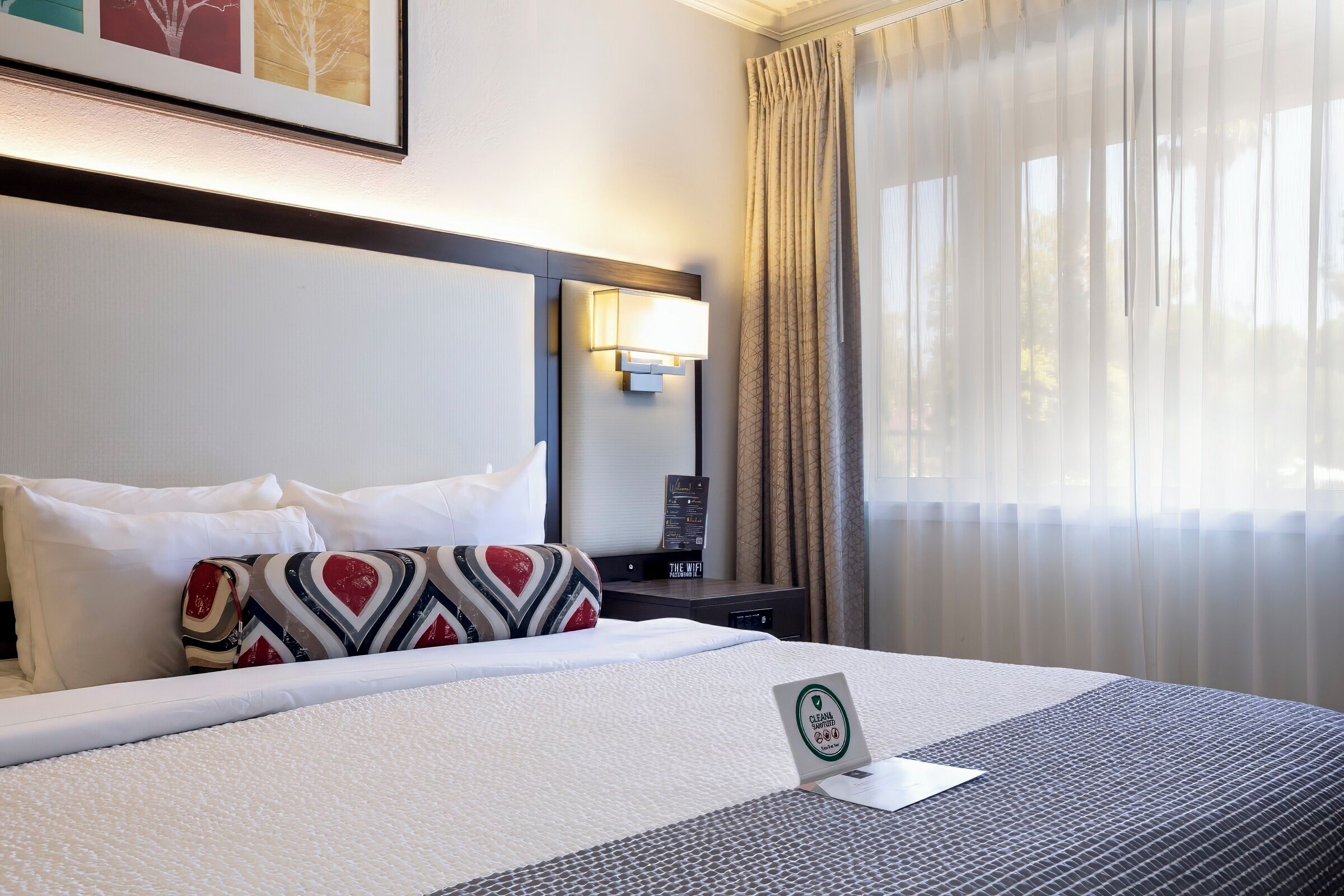 Une chambre d’hôtel avec un lit bien fait, une lampe de chevet, une table de chevet et une fenêtre avec des rideaux.