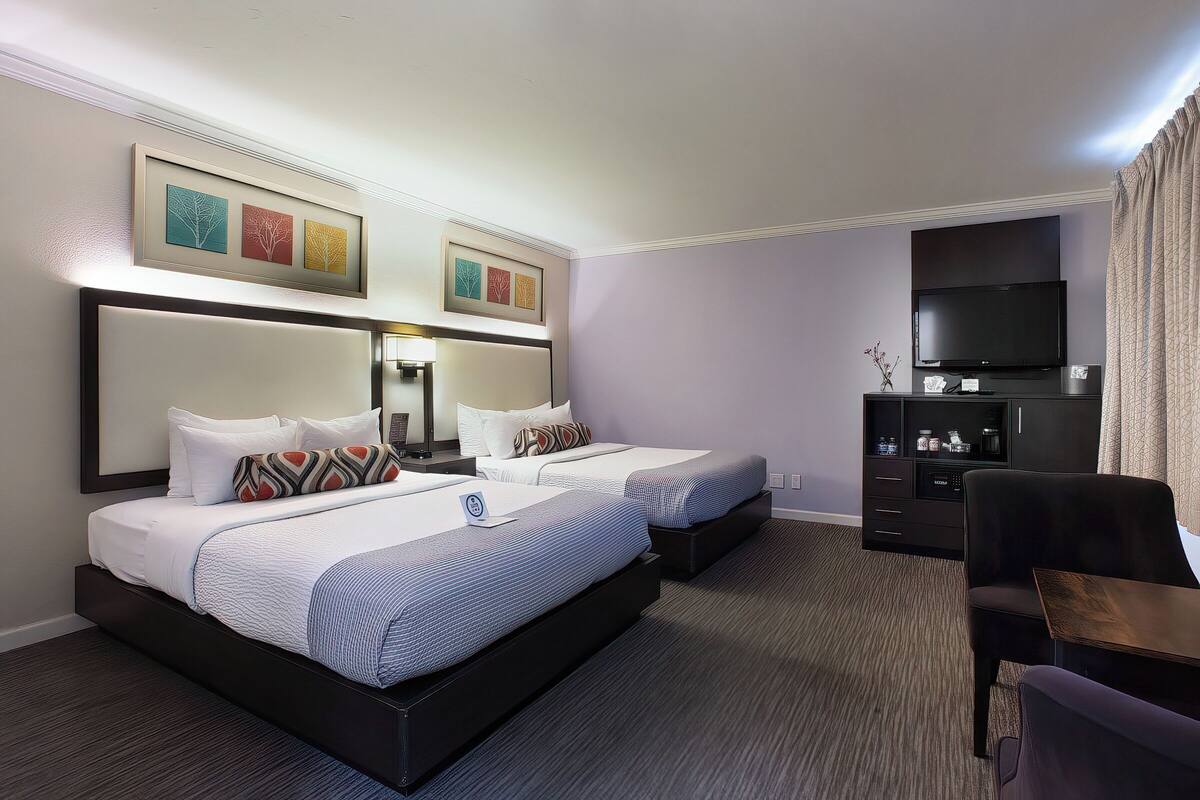 A hotel room with two beds, a TV, a desk, and a bookshelf.