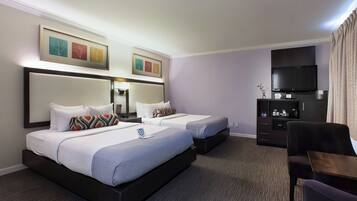 A hotel room with two beds, a TV, a desk, and a bookshelf.