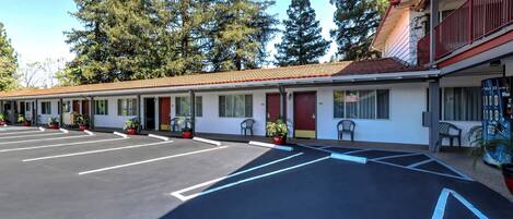 A motel with a parking lot, potted plants, and a building with a red roof.