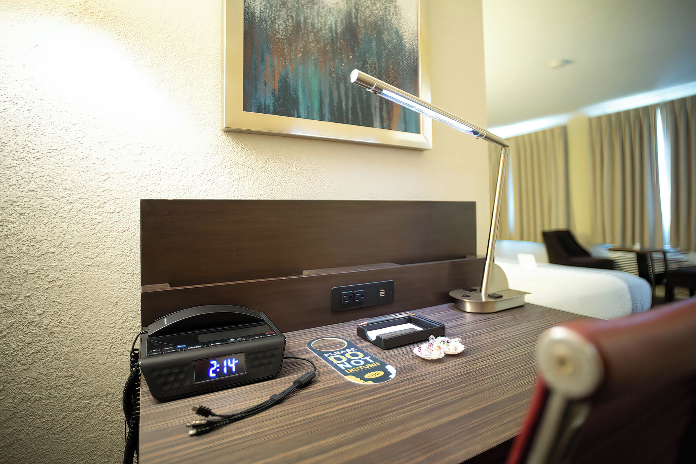 Escritorio de habitación de hotel con un reloj digital, una lámpara de escritorio, un teléfono y un cartel que dice 'No molestar'.