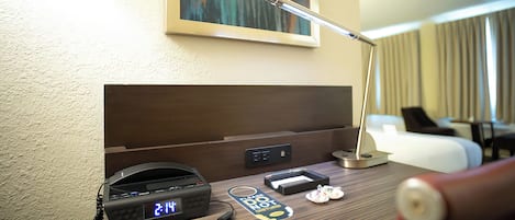 A hotel room desk with a digital clock, a desk lamp, a phone, and a "Please do not disturb" sign.