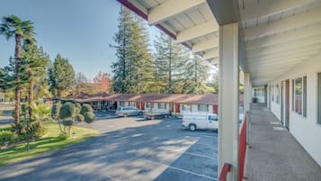 A motel with a covered parking area, a row of rooms with a red roof, and a parking lot with several cars.