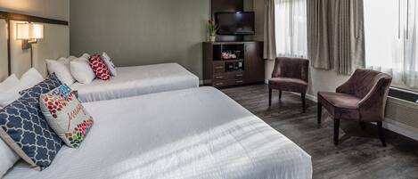 A hotel room with two beds, a TV, a chair, and a cabinet with a plant.