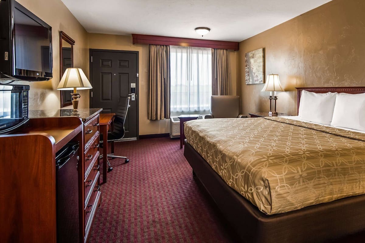 A hotel room with a bed, desk, chair, television, and lamps.