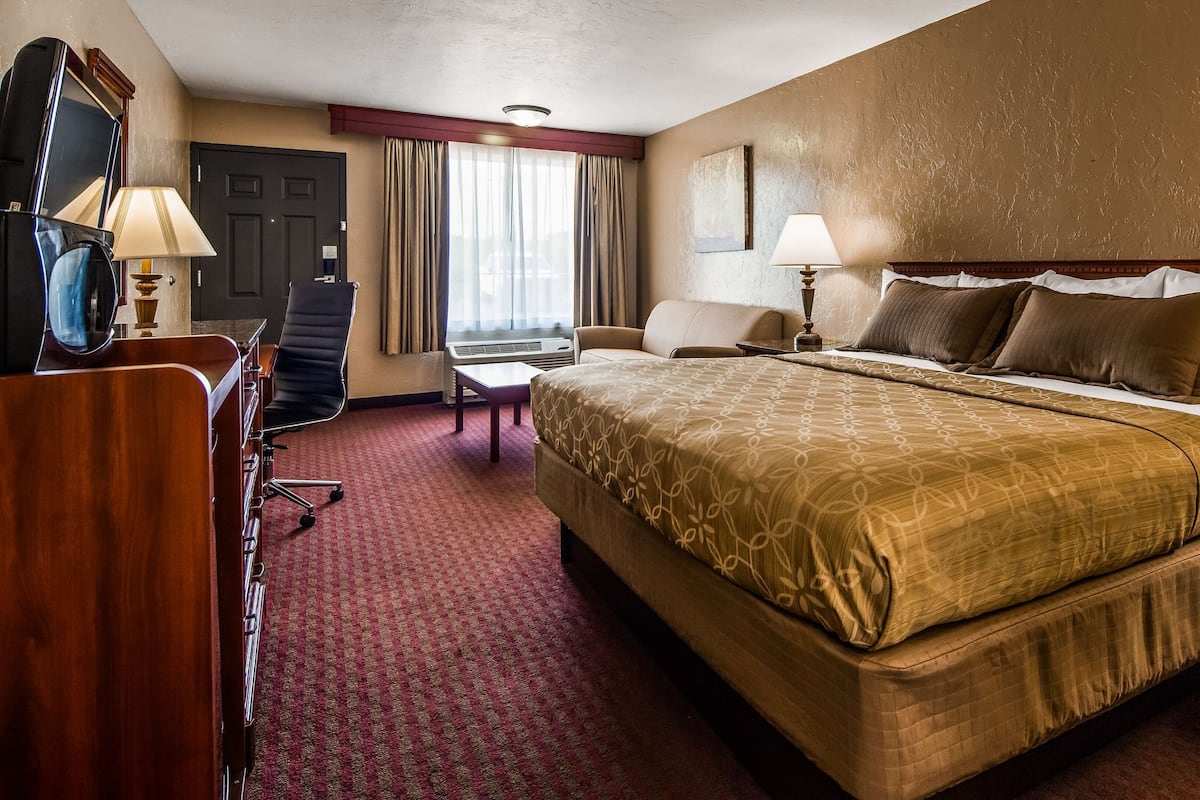 A hotel room with a large bed, a desk with a chair, a small table, and a window with curtains.