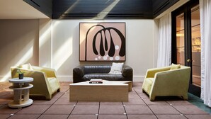 A modern living room with a black leather sofa, two yellow armchairs, a coffee table, and a large abstract painting on the wall. - Kimpton Alton Fisherman's Wharf by IHG (San Francisco)