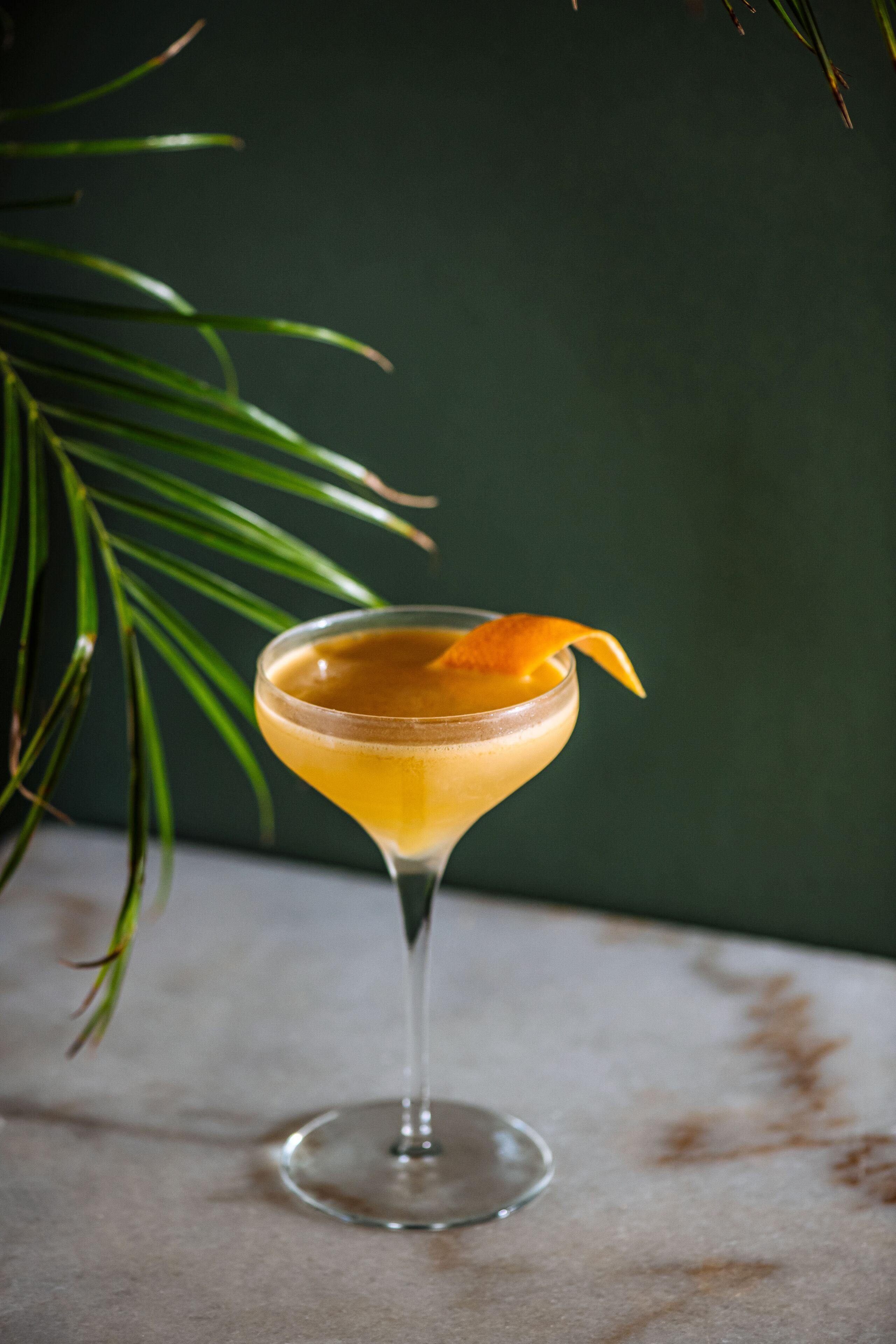 A cocktail in a martini glass with an orange garnish on a marble surface.