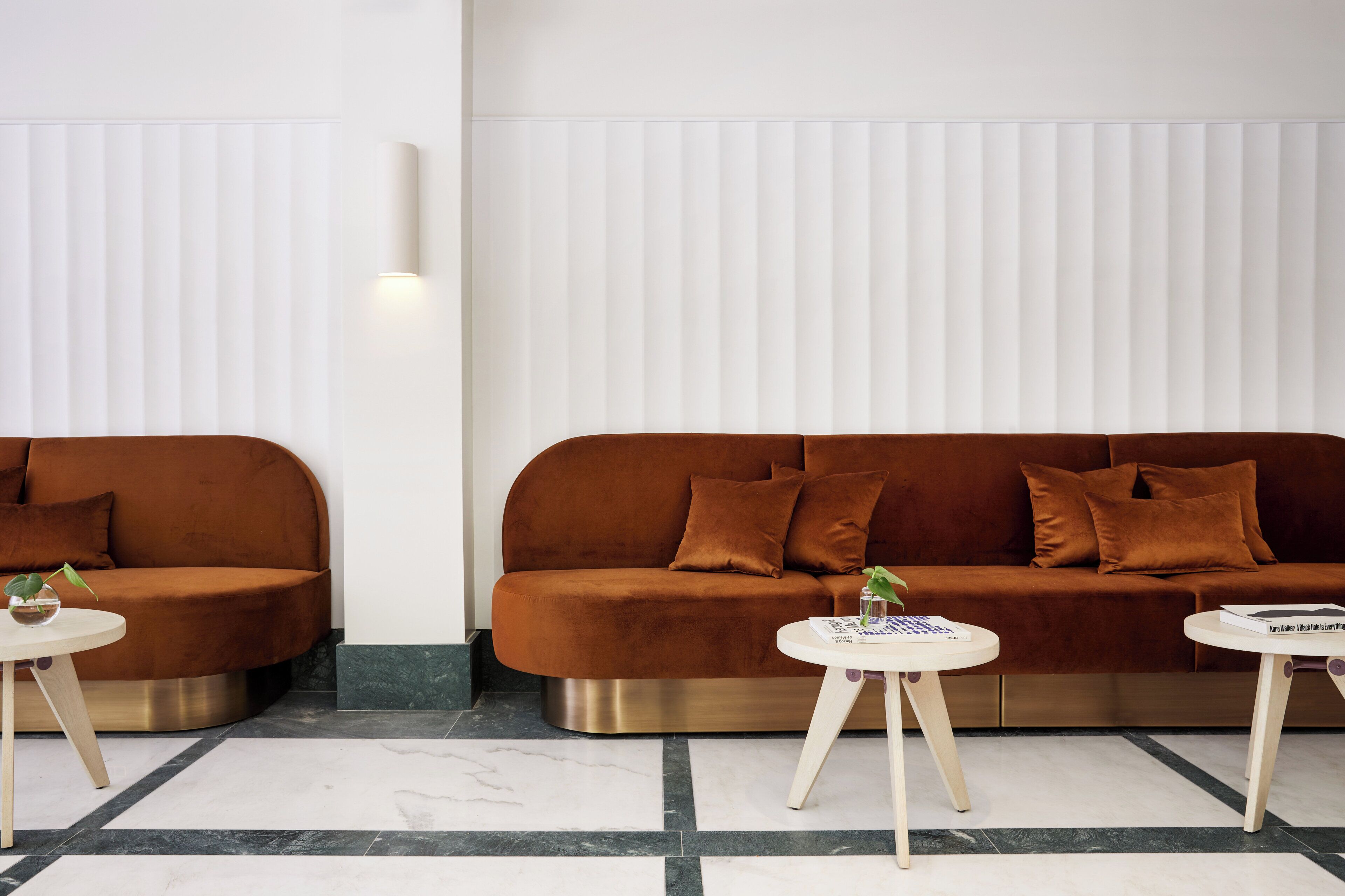 Uma sala de estar moderna com dois sofás, uma luminária fixada na parede e uma pequena mesa com um livro.