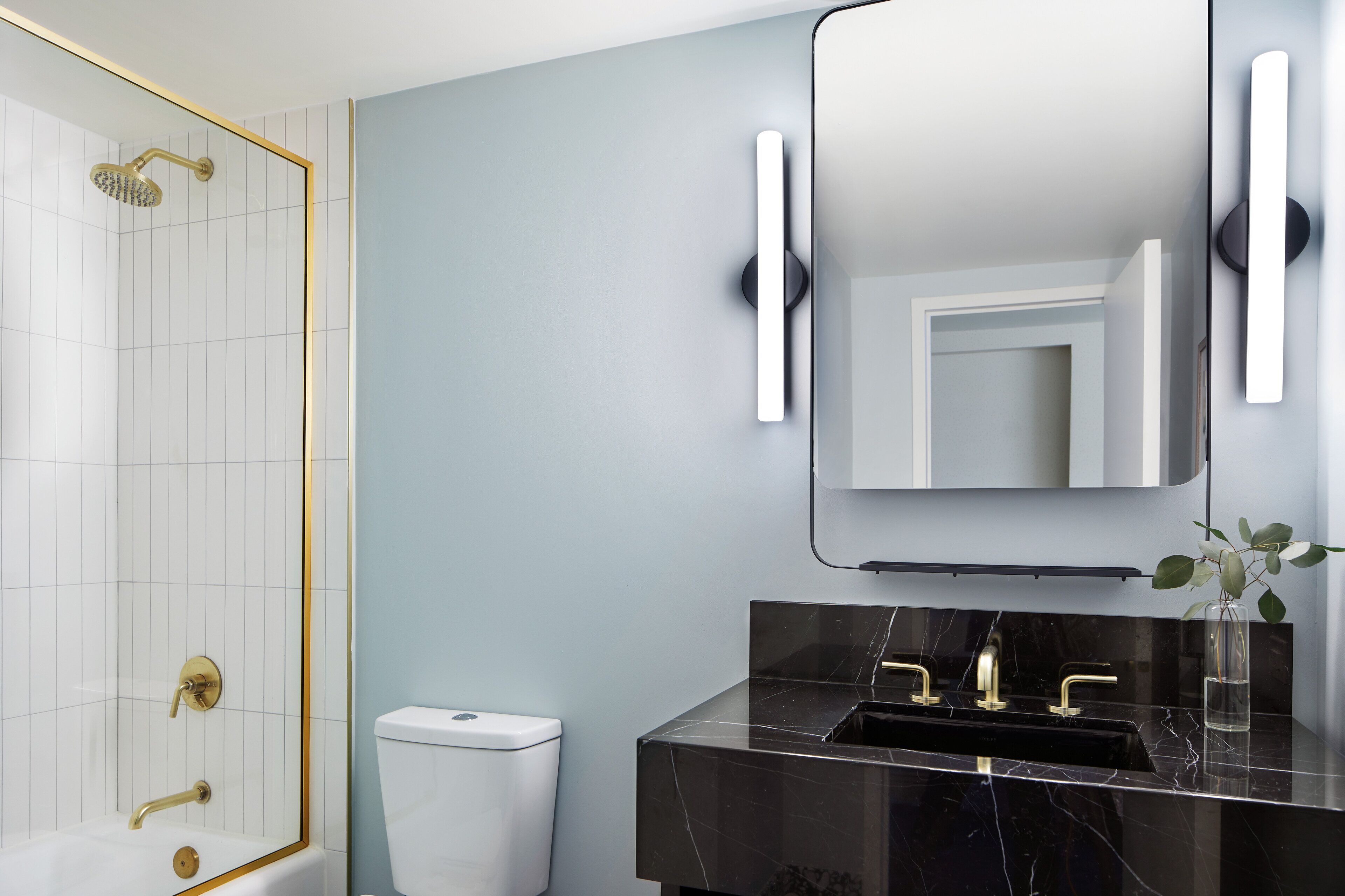 Un baño moderno con ducha envuelta en vidrio, lavamanos de mármol negro y un espejo grande con apliques de pared.