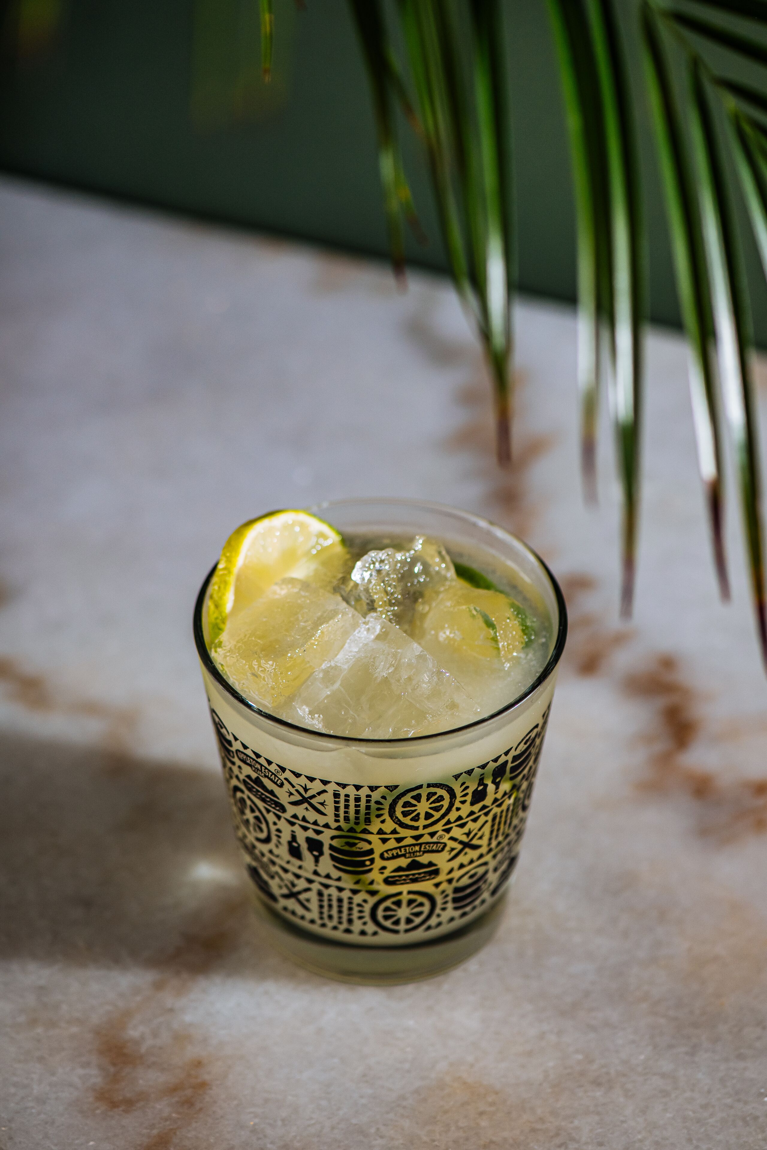 A glass with ice and lime slices on a marble surface.