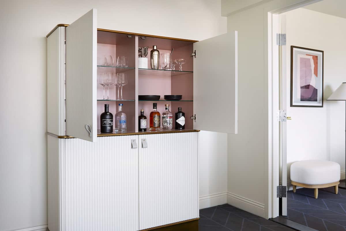 A white cabinet with glass shelves containing bottles and glasses.