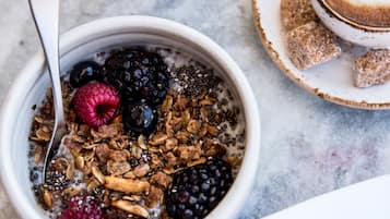 Eine Schüssel mit Granola und Beeren, ein Glas Orangensaft und eine Tasse Kaffee auf einer Marmorplatte.