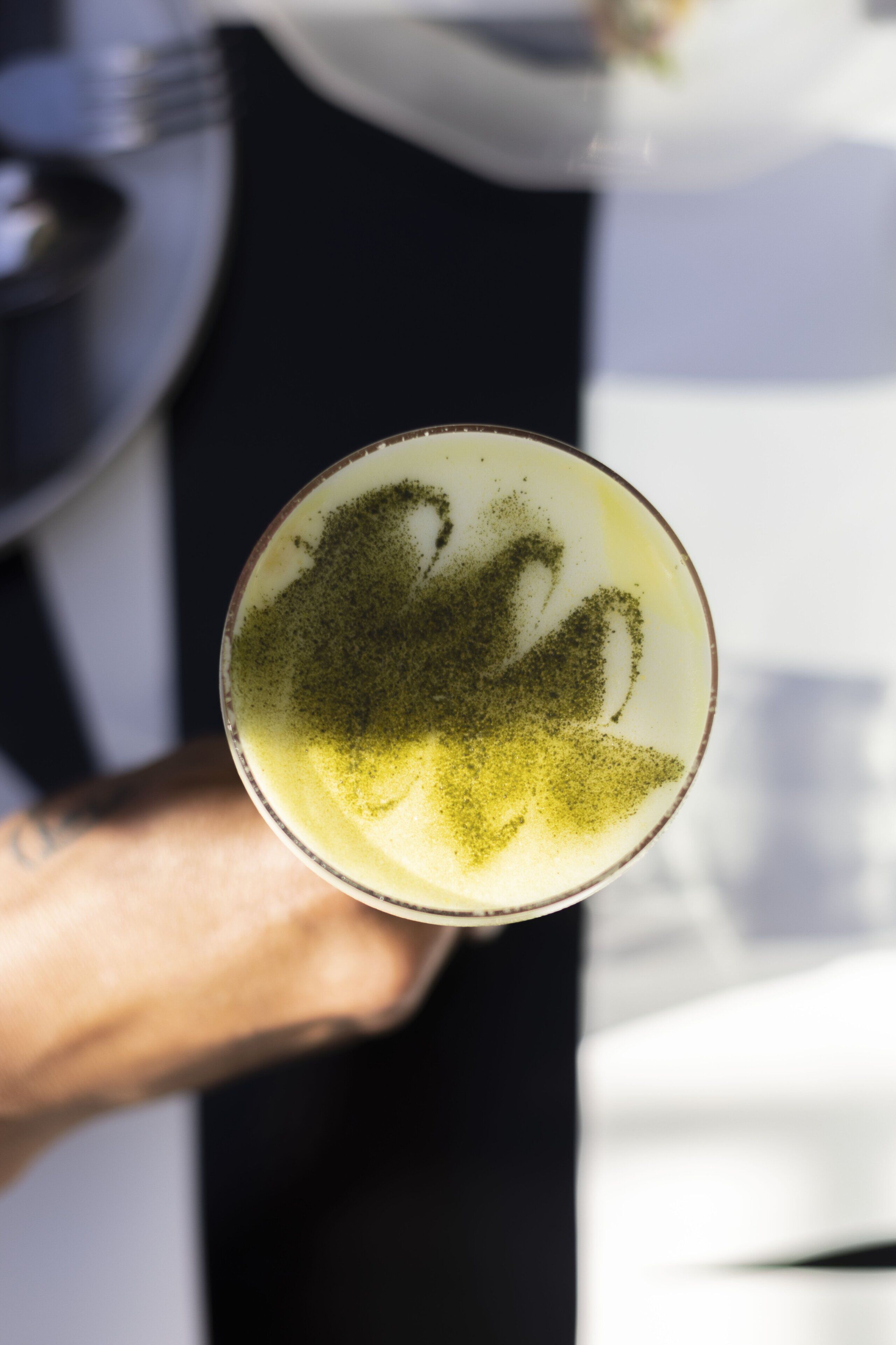 Un gros plan d’une boisson surmontée d’une mousse crémeuse et ornée d’un motif en forme de feuille, tenue par une personne.