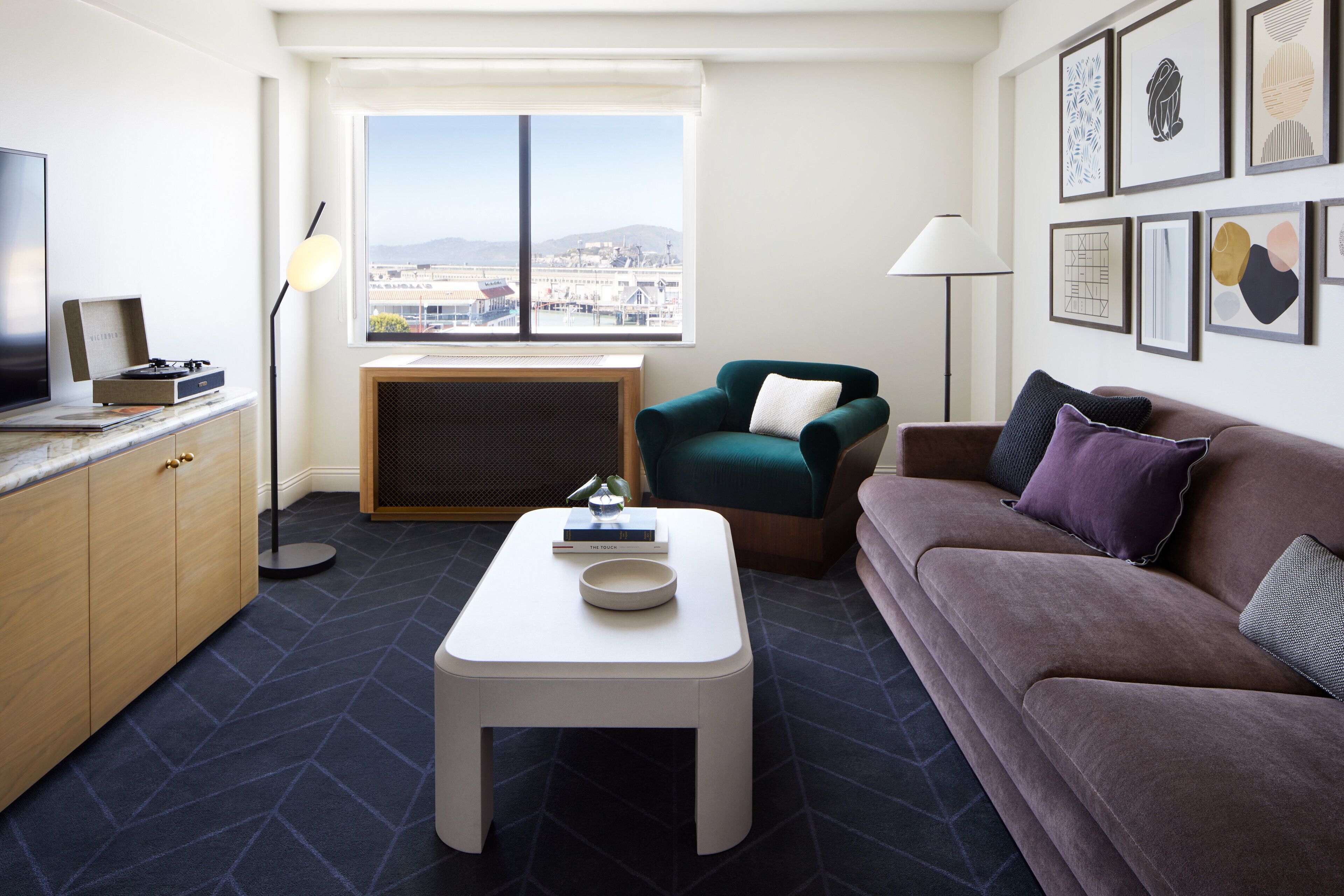 Una sala de estar moderna con un sofá, una mesa de centro, un televisor y vistas de la ciudad a través de amplios ventanales.