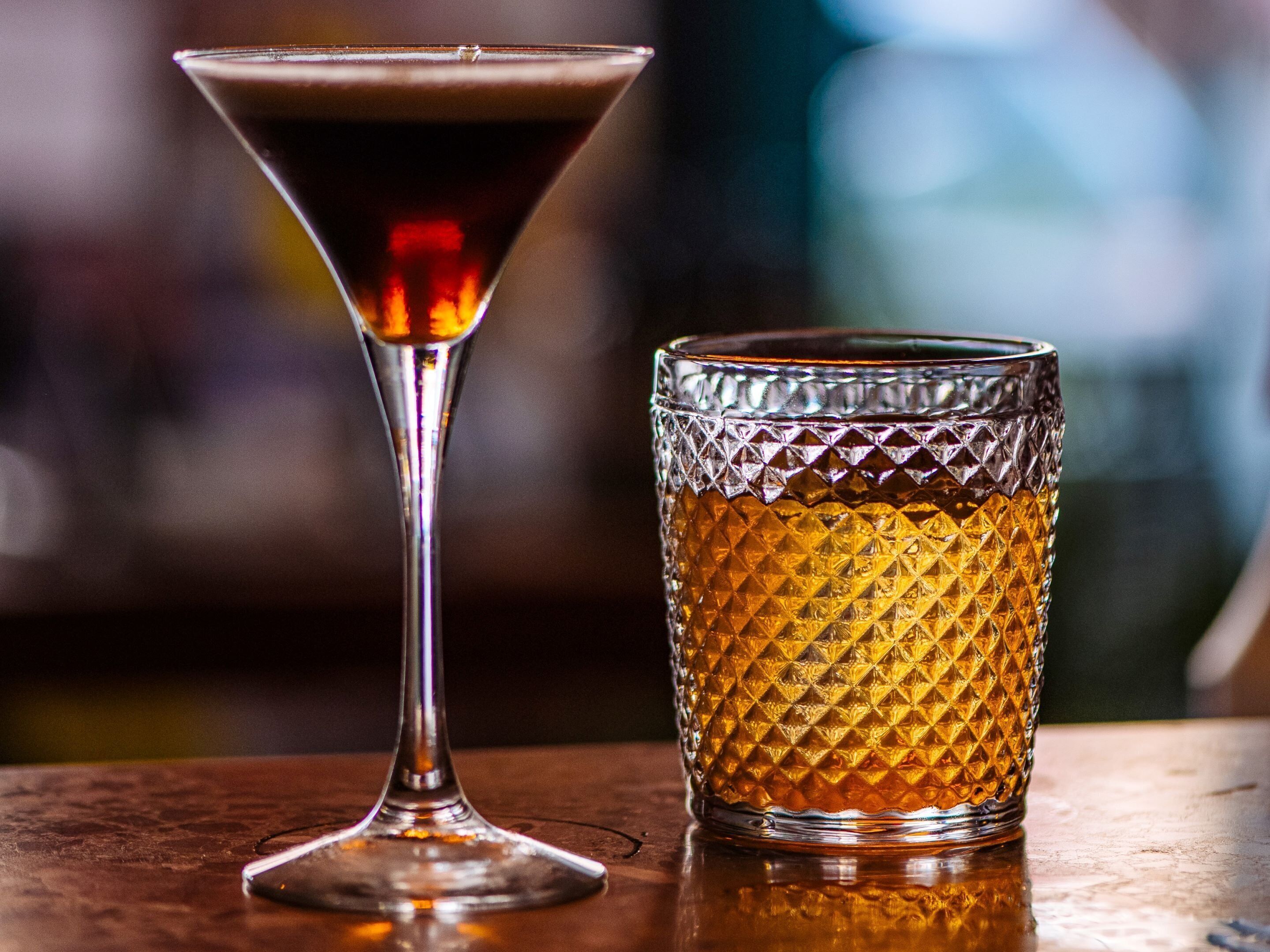 Um copo de martini e um copo texturizado sobre uma superfície de madeira.