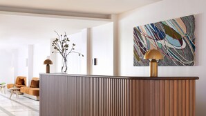 A reception area with a wooden reception desk, a modern lamp, a colorful abstract painting, and a seating area with sofas and a small table. - Kimpton Alton Fisherman's Wharf by IHG (San Francisco)