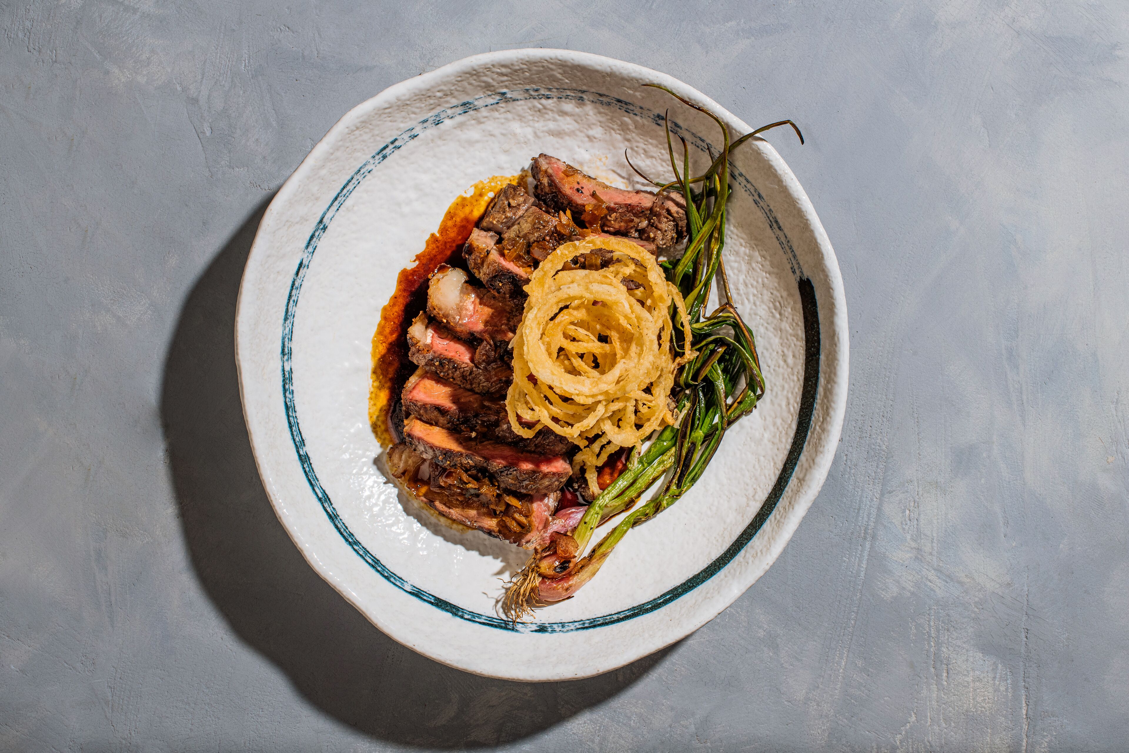Un plato de bistec con cebollas y espárragos sobre una superficie gris texturizada.