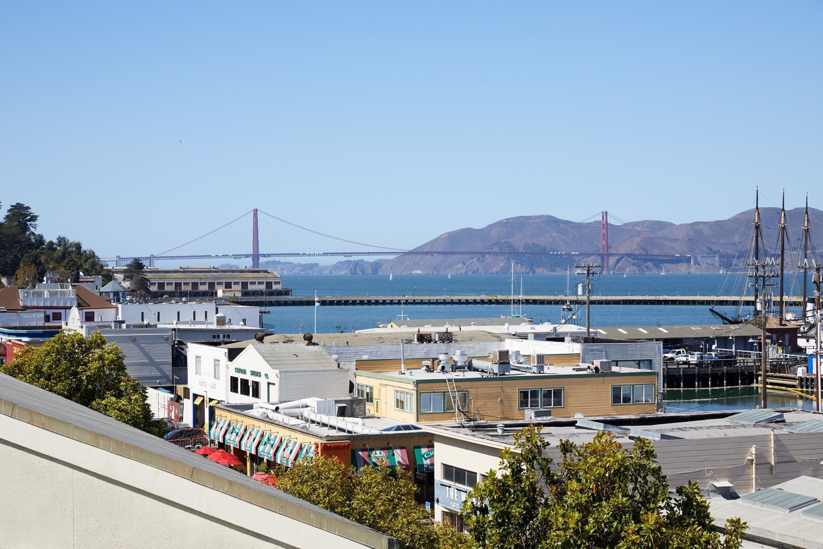 A coastal cityscape with a prominent bridge in the background, a marina with boats, and various buildings including a restaurant.