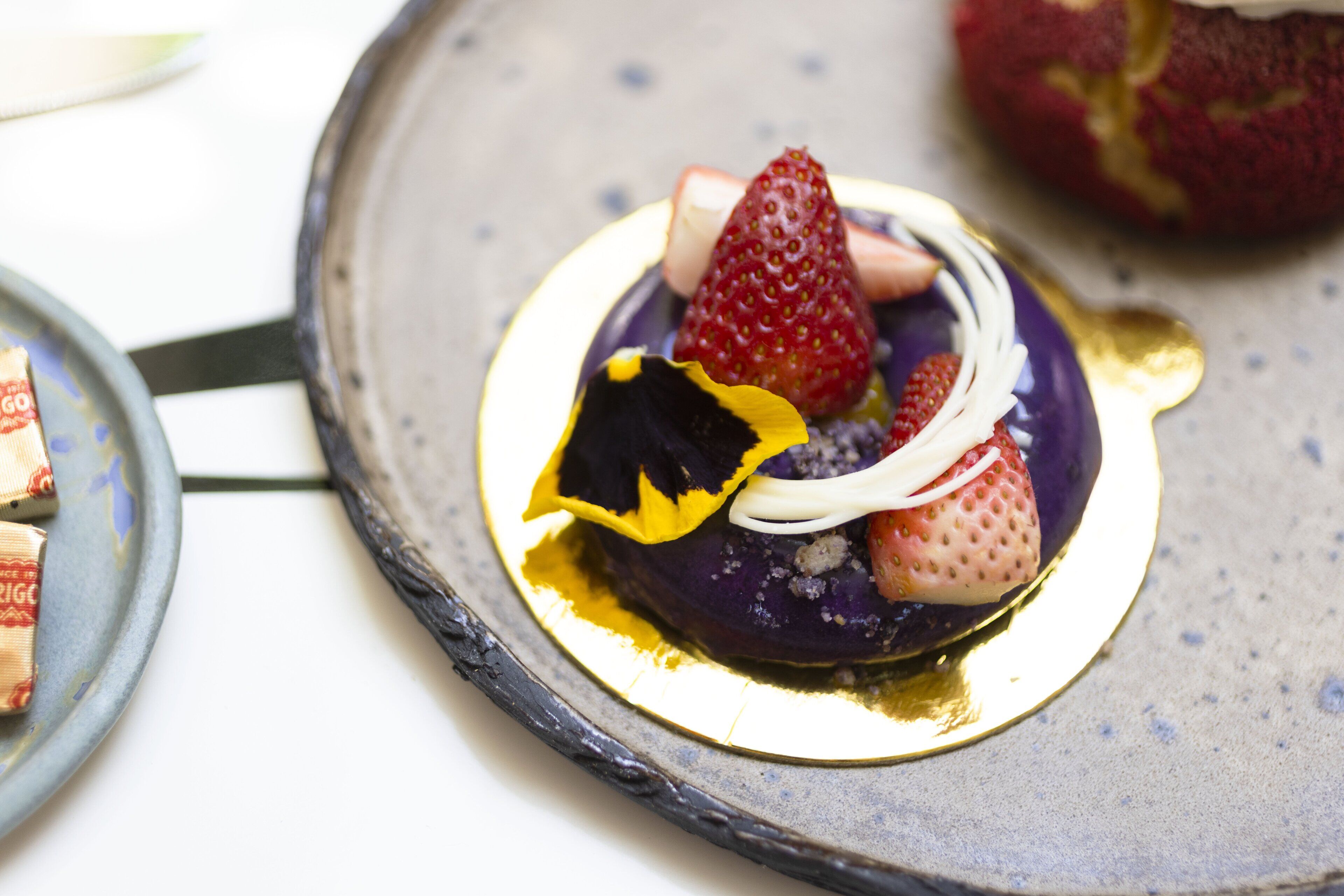 Une assiette à dessert à la base violette, garnie de fraises et surmontée d’une feuille jaune.