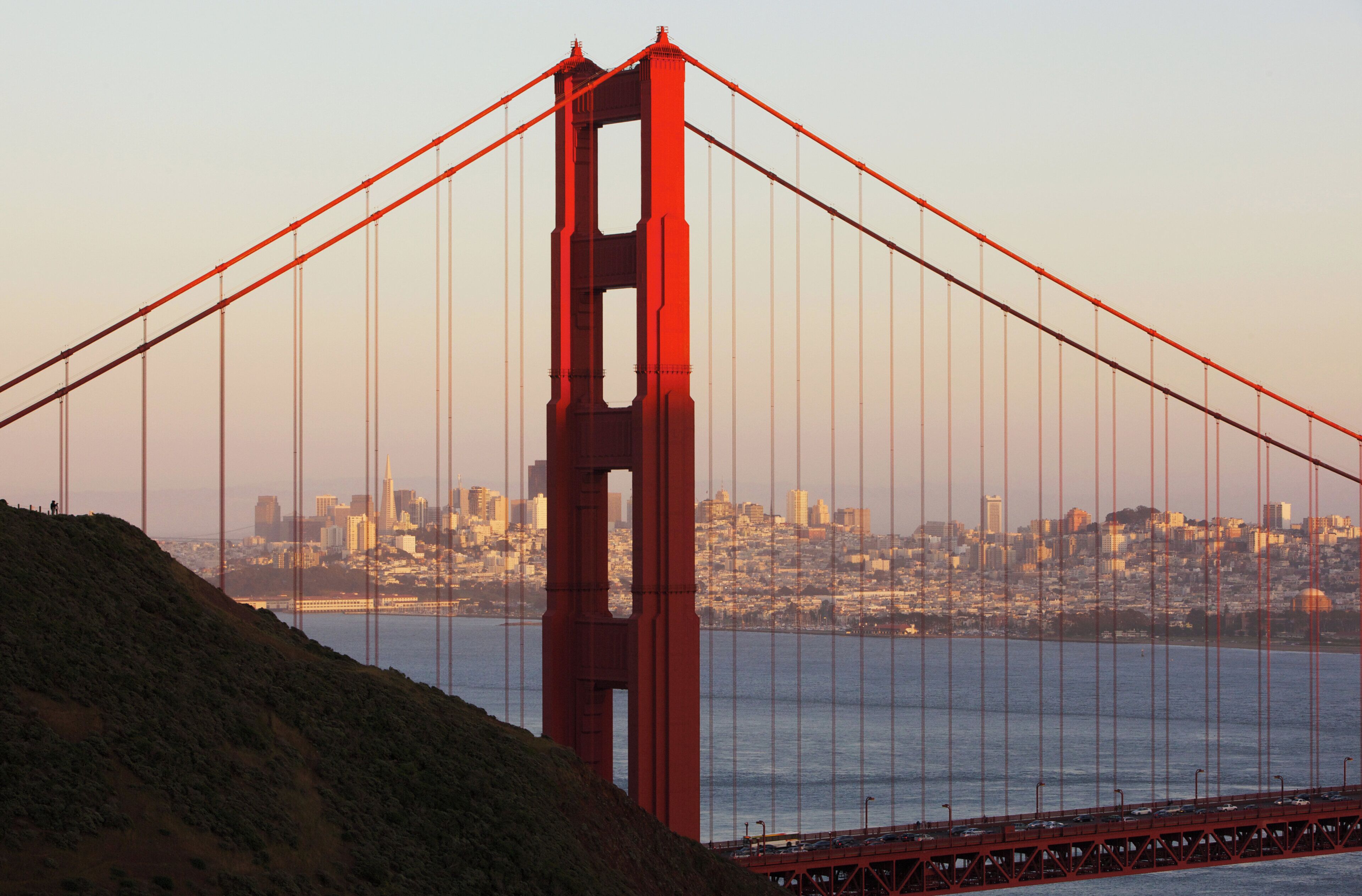 A large suspension bridge with a prominent tower, spanning over a body of water with a cityscape in the background.