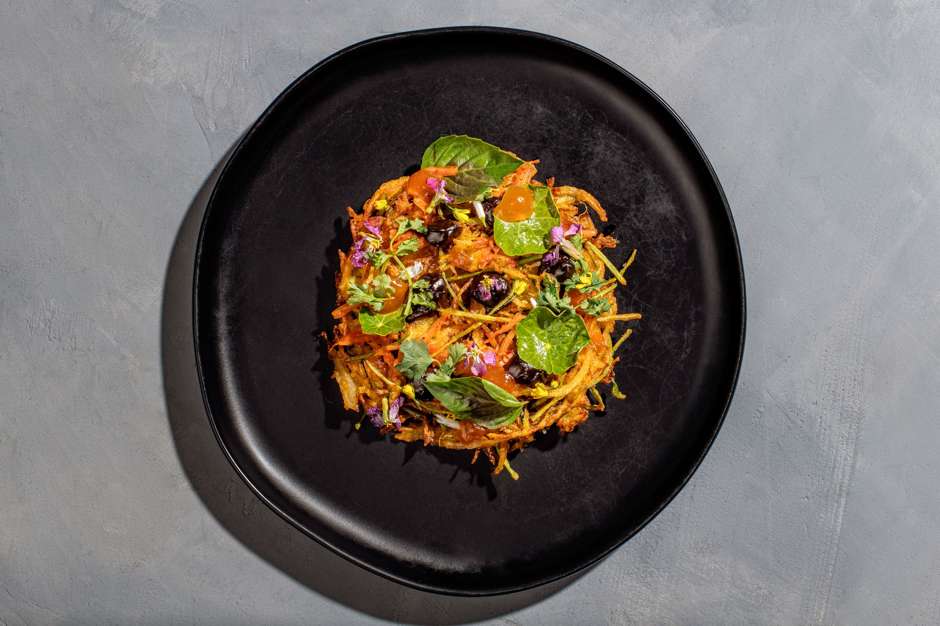 A black plate with a colorful dish on a textured gray surface.
