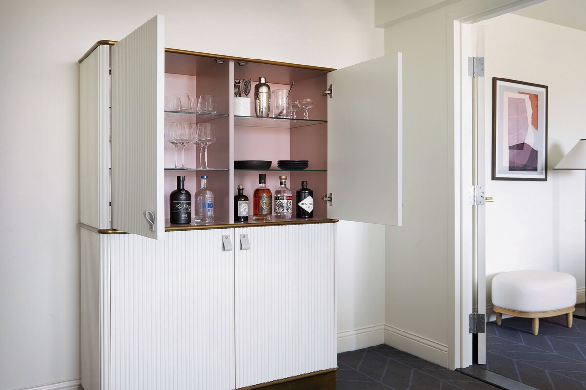 A white cabinet with glass shelves containing bottles and glasses.