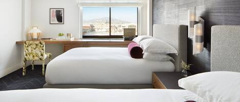 A hotel room with two beds, a desk, a chair, and a large window with a city view.