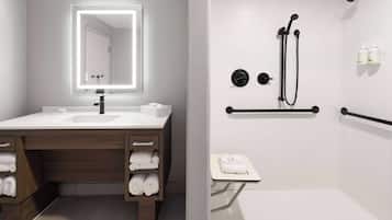 A modern bathroom with a vanity, a large mirror, a shower with a handheld showerhead, and a towel rack.