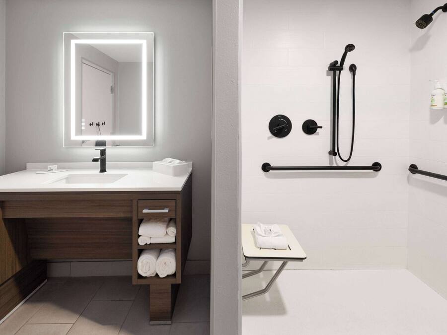 A modern bathroom with a vanity, a large mirror, a shower with a handheld showerhead, and a towel rack.