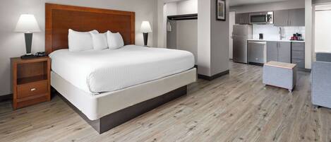 A hotel room with a large bed, a nightstand, a desk, a kitchenette, and a wardrobe.