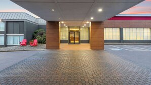 A hotel entrance with a paved walkway, red chairs, and a glass door entrance.