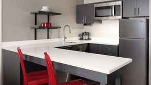 A modern kitchen with a large island, stainless steel appliances, and red chairs.