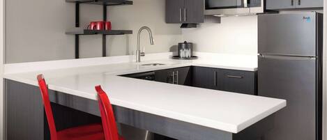 A modern kitchen with a large island, stainless steel appliances, and red chairs.