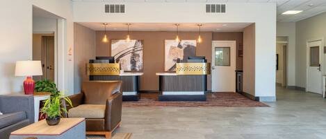 A hotel lobby with a reception desk, seating area, and a plant.
