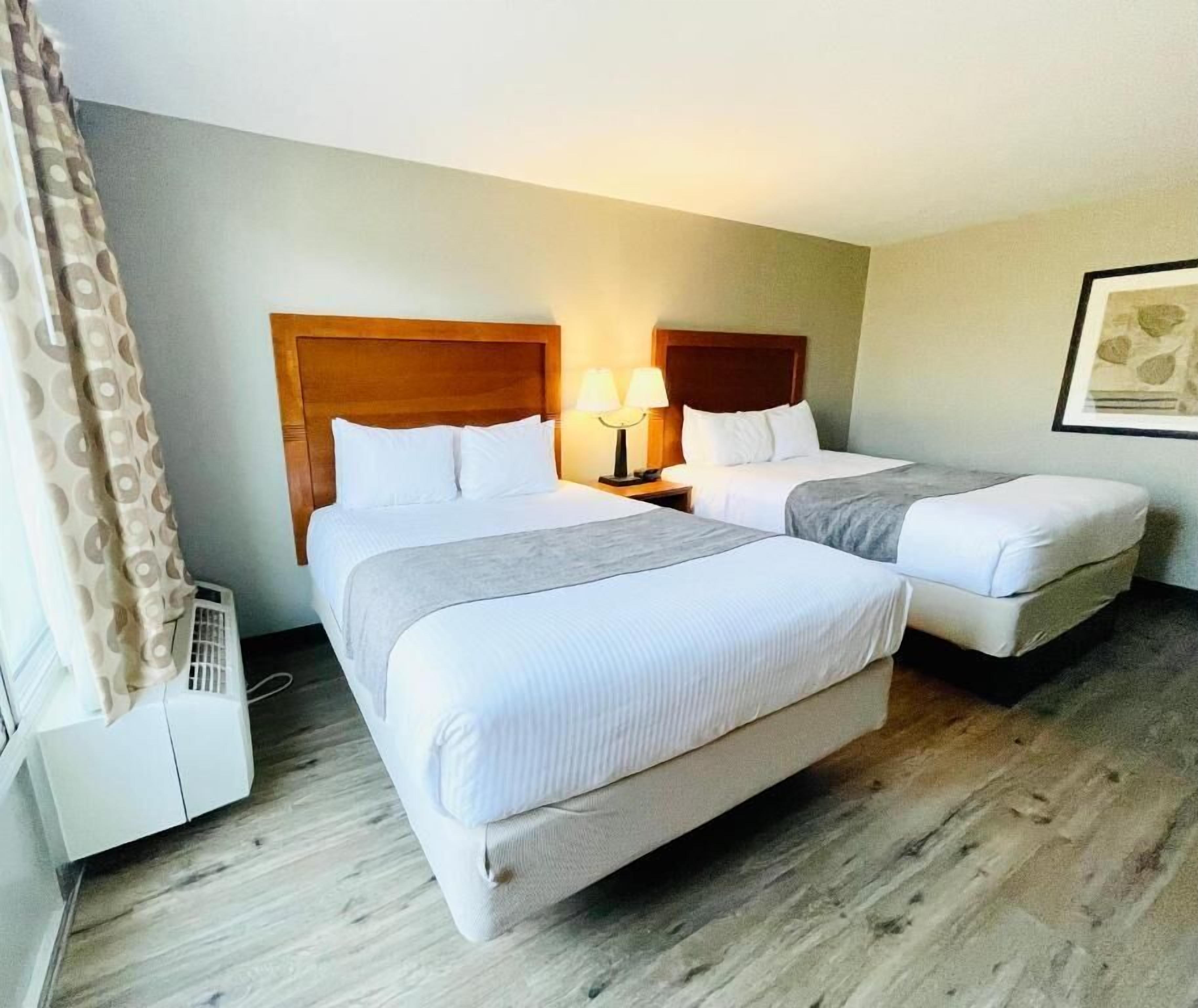 Een hotelkamer met twee bedden, een houten hoofdeinde, een nachtkastje met een lamp en een lijst met een afbeelding aan de muur.