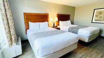A hotel room with two beds, a wooden headboard, a bedside table with a lamp, and a framed picture on the wall.