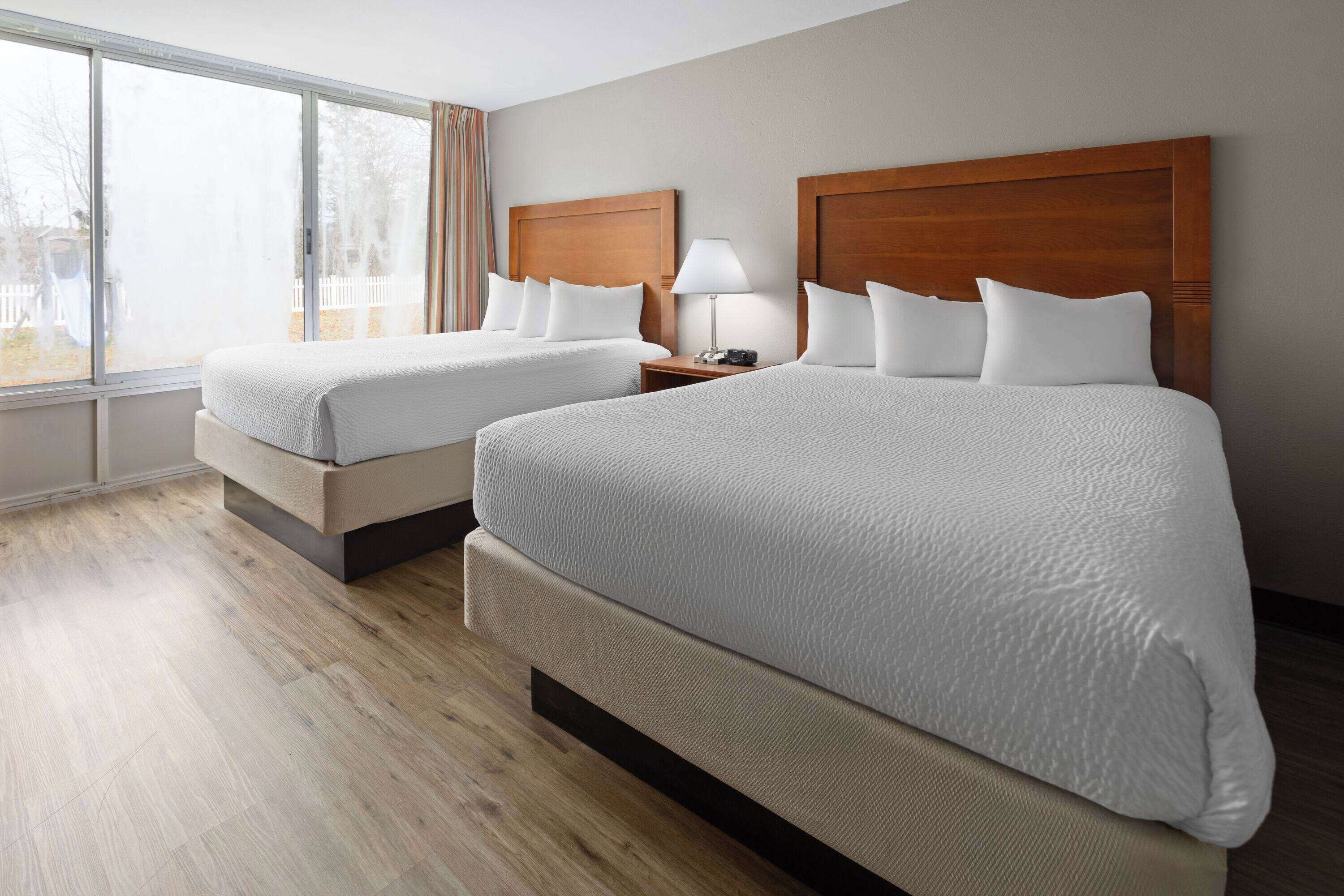Habitación de hotel con dos camas, un ventanal grande y piso de madera.