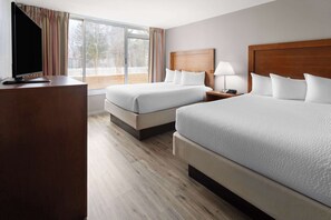 A hotel room with two beds, a TV, and a large window with curtains.