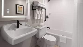 Une salle de bain moderne avec un lavabo, des toilettes et une baignoire, tous de couleur blanche. On y trouve un porte-serviettes avec des serviettes pliées et un tableau encadré accroché au mur.