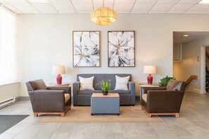 Uma sala de estar moderna com um sofá cinzento, duas poltronas, uma mesa de centro e duas pinturas abstratas.