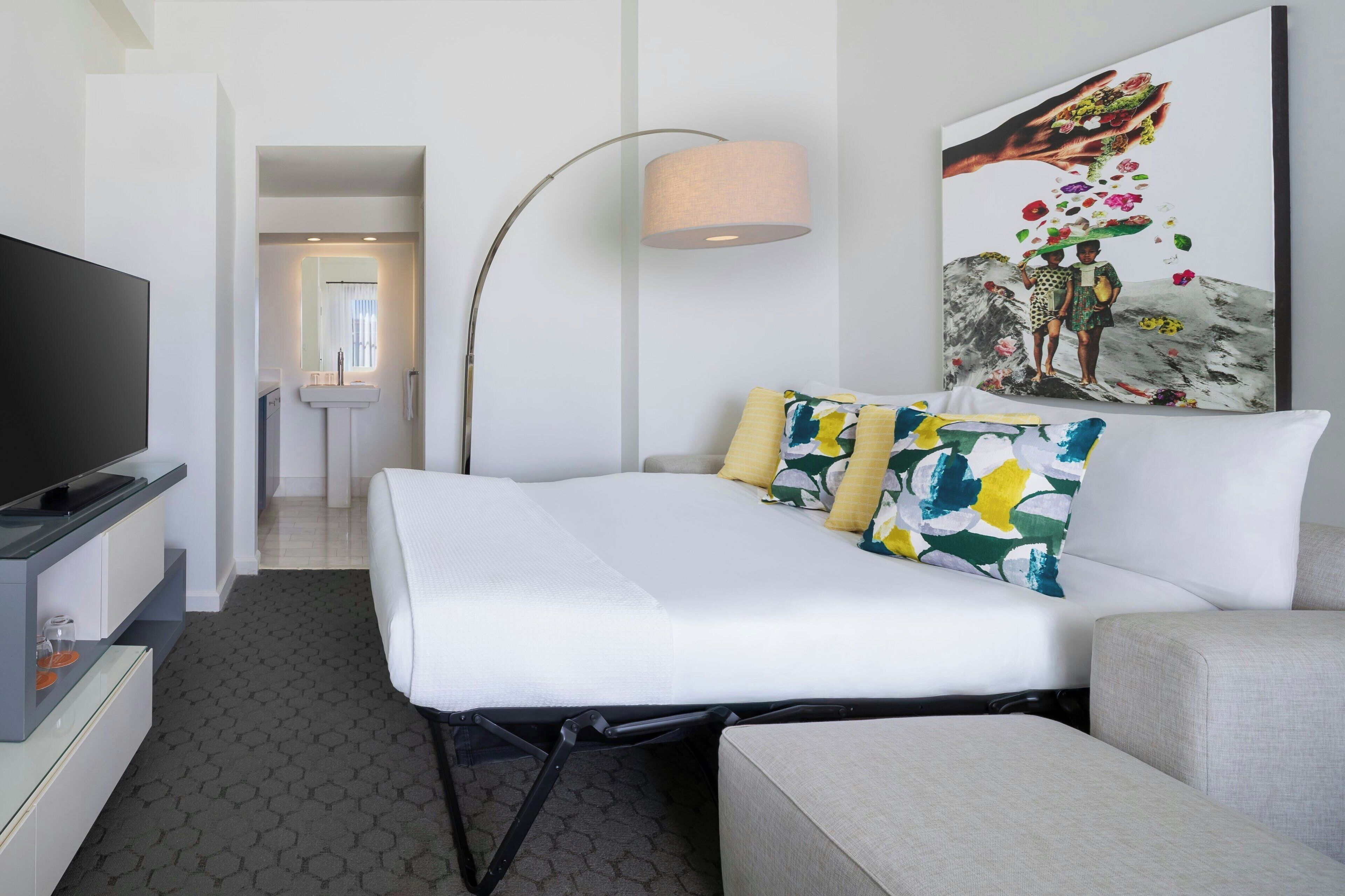A hotel room with a bed, a TV, a desk, and a lamp.