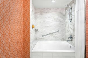 Un baño con una bañera blanca, una ducha con cabezal de ducha manual y un perchero para toallas.