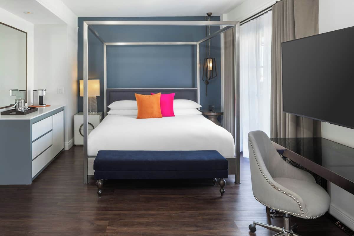A modern hotel room with a large bed, a desk with a chair, a TV, and a window with curtains.