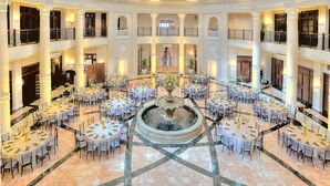 A spacious atrium with multiple dining tables arranged around a central fountain, featuring a grand staircase in the background. - Hotel Colonnade Coral Gables, Autograph Collection (Coral Gables)