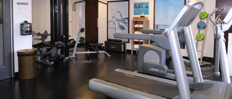 A gym with cardio machines, weight training equipment, and a poster on the wall.